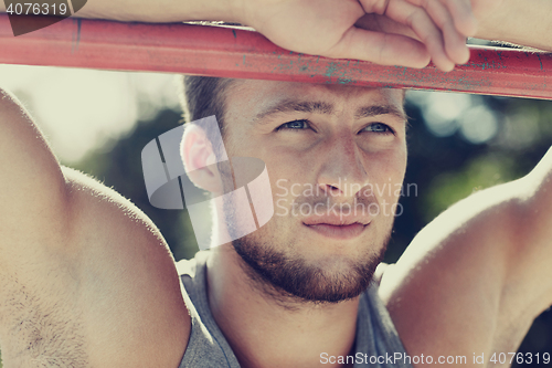 Image of young man exercising on horizontal bar outdoors