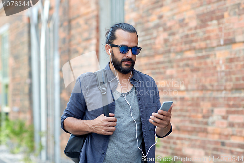 Image of man with earphones and smartphone walking in city