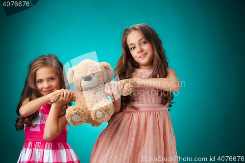 Image of The two cute little girls on blue background with Teddy bear