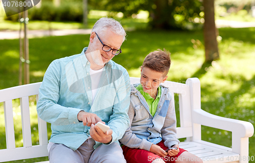 Image of old man and boy with smartphones at summer park