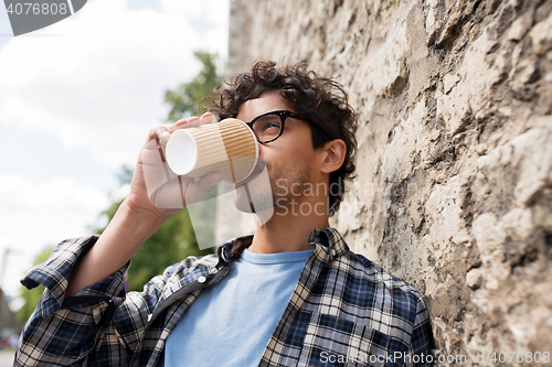 Image of man in eyeglasses drinking coffee over street wall