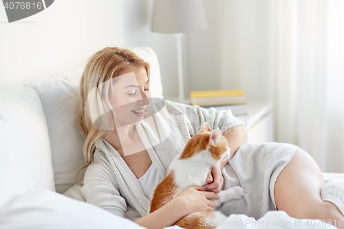 Image of happy young woman with cat in bed at home