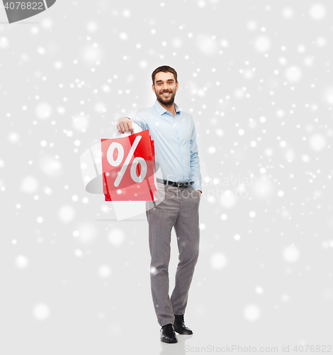 Image of smiling man with red shopping bag over snow