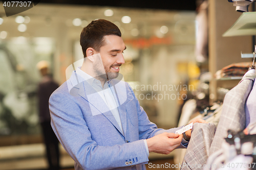 Image of happy young man choosing clothes in clothing store