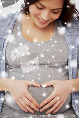 Image of happy pregnant woman making heart gesture at home