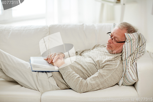 Image of senior man sleeping on sofa with book at home