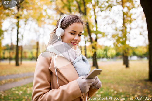 Image of woman with smartphone and earphones in autumn park