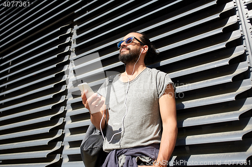 Image of man with earphones and smartphone on city street