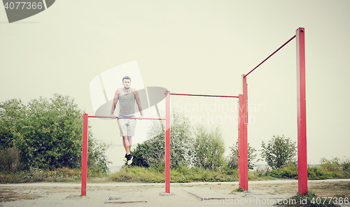 Image of young man exercising on horizontal bar outdoors