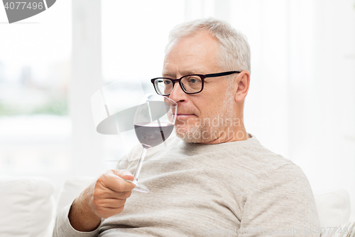 Image of senior man drinking red wine from glass at home