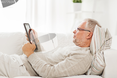 Image of senior man with tablet pc lying on sofa at home