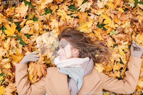 Image of beautiful happy woman lying on autumn leaves