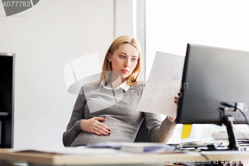 Image of pregnant businesswoman reading papers at office