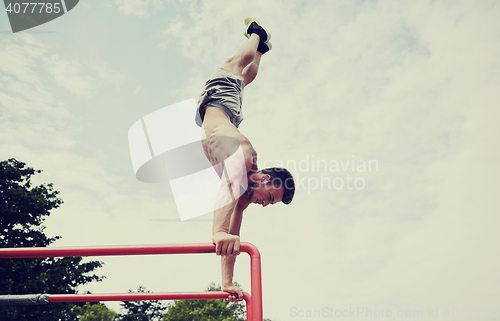 Image of young man exercising on parallel bars outdoors