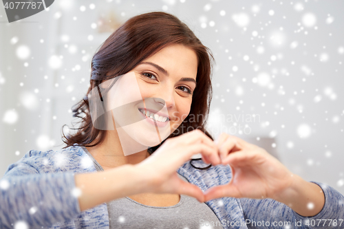 Image of happy young woman showing heart with hands at home