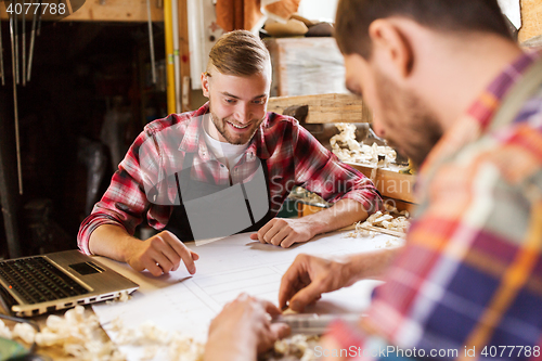 Image of carpenters with laptop and blueprint at workshop