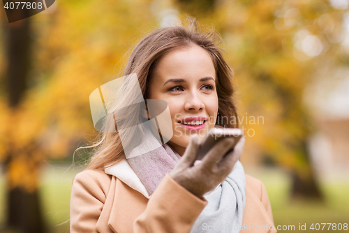 Image of woman recording voice on smartphone in autumn park