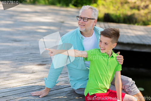 Image of grandfather and grandson sitting on river berth