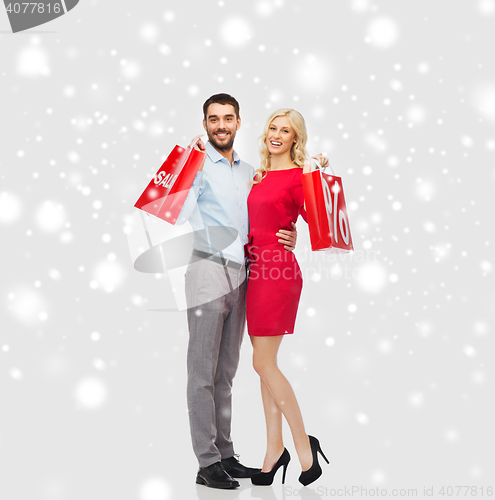 Image of happy couple with red shopping bags over snow