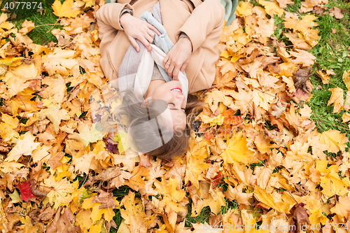 Image of beautiful happy woman lying on autumn leaves