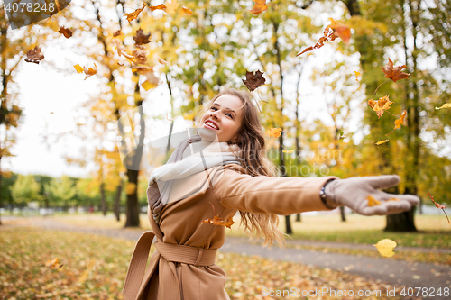 Image of happy woman having fun with leaves in autumn park