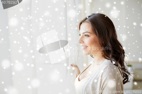 Image of happy young woman looking through window at home