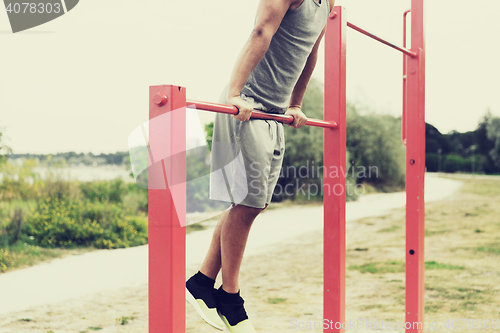 Image of young man exercising on horizontal bar outdoors