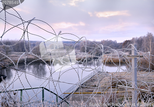 Image of Post a fence of barbed wire in winter in frost at dawn