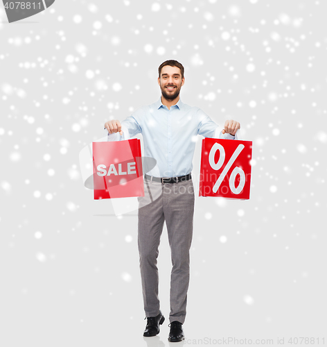 Image of smiling man with red shopping bags over snow