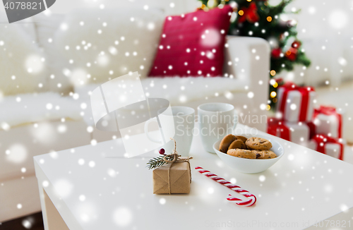 Image of close up of gift, sweets and cups on table at home