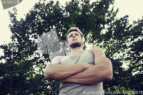 Image of sporty young man with crossed arms at summer park