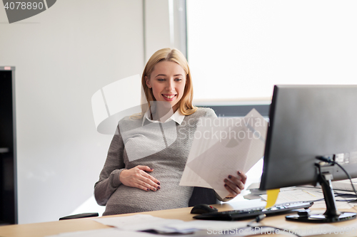 Image of pregnant businesswoman reading papers at office