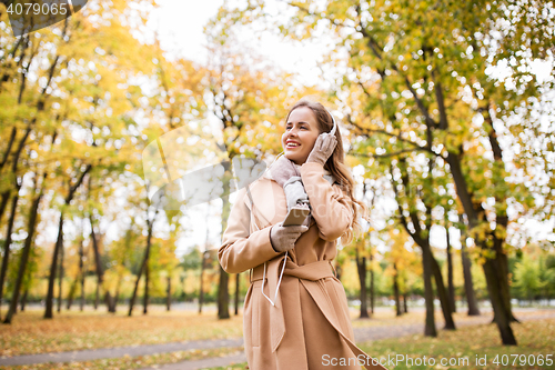 Image of woman with smartphone and earphones in autumn park