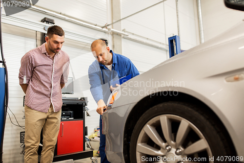 Image of auto mechanic with clipboard and man at car shop