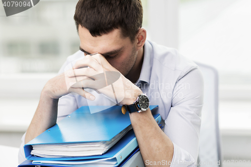 Image of sad businessman with stack of folders at office