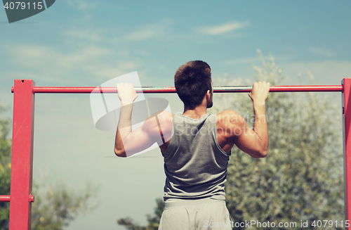 Image of young man exercising on horizontal bar outdoors