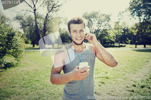Image of happy man with earphones and smartphone at park