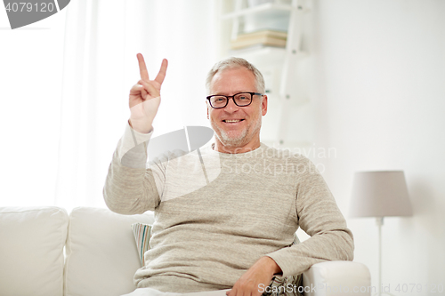 Image of smiling senior man showing v sign at home