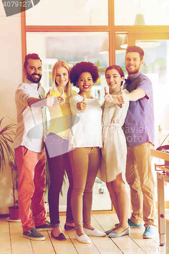 Image of happy creative team showing thumbs up in office