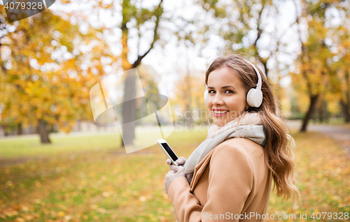 Image of woman with smartphone and earphones in autumn park