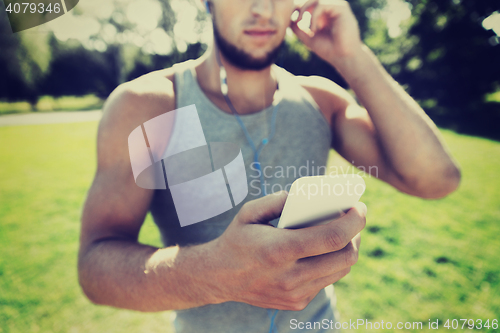 Image of young man with earphones and smartphone at park