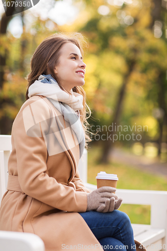 Image of happy young woman drinking coffee in autumn park