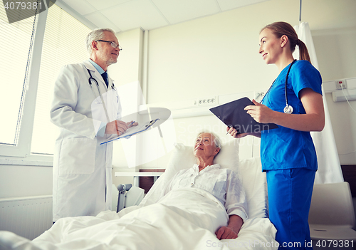 Image of doctor and nurse visiting senior woman at hospital