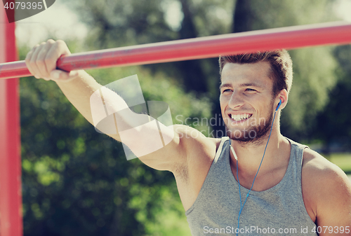 Image of happy young man with earphones and horizontal bar