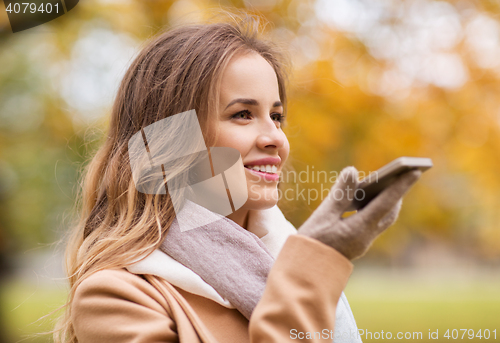 Image of woman recording voice on smartphone in autumn park