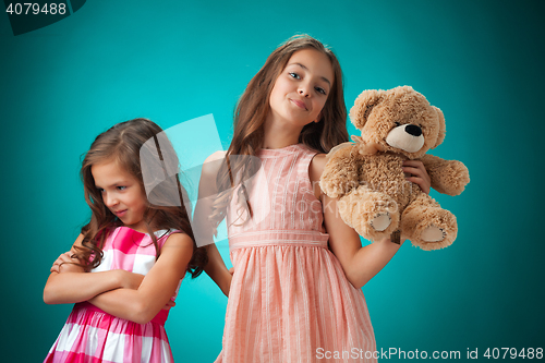 Image of The two cute little girls on blue background with Teddy bear