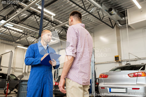 Image of auto mechanic with clipboard and man at car shop