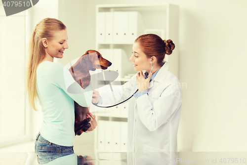 Image of happy woman with dog and doctor at vet clinic