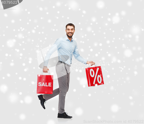 Image of smiling man with red shopping bags over snow