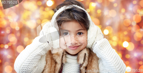 Image of happy little girl in earmuffs over holidays lights